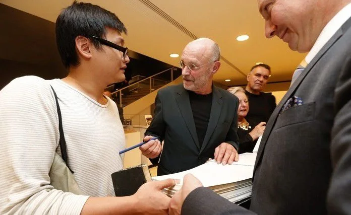 Albright-Knox Art Gallery director Janne Sirén, right, holds a book as Anselm Kiefer, center, autographs it for Shen Linghao